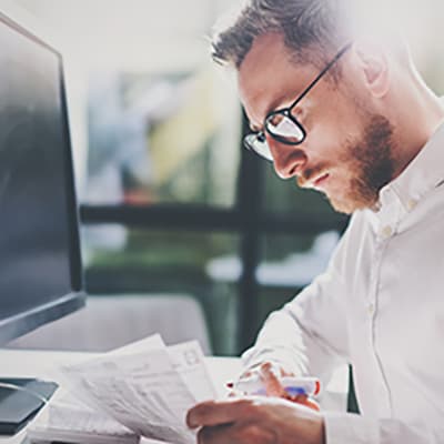 Stock image of office employee handling paper and highlighter in front of a monitor.