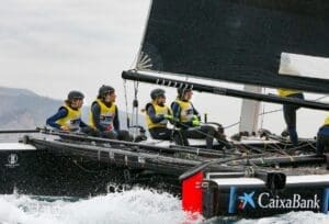 4 women sailing on a large luxury superyacht catamaran out at sea. They are all wearing matching black helmets and yellow life jackets.