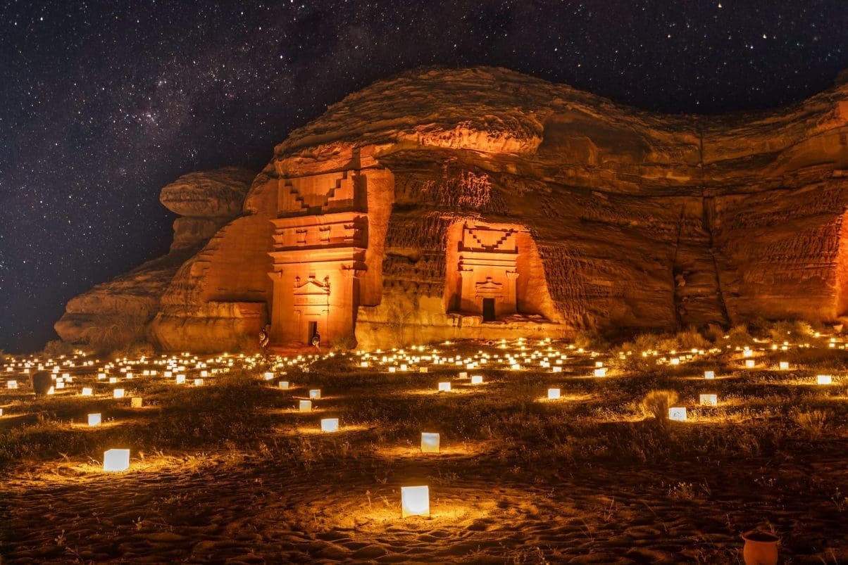 Saudi monument at night surrounded by lots of candle lights in the sands under a starry sky